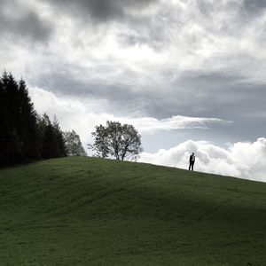 People standing on grassy field against cloudy sky