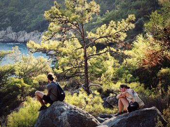 People sitting on rock against trees