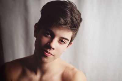 Close-up portrait of shirtless boy against curtain