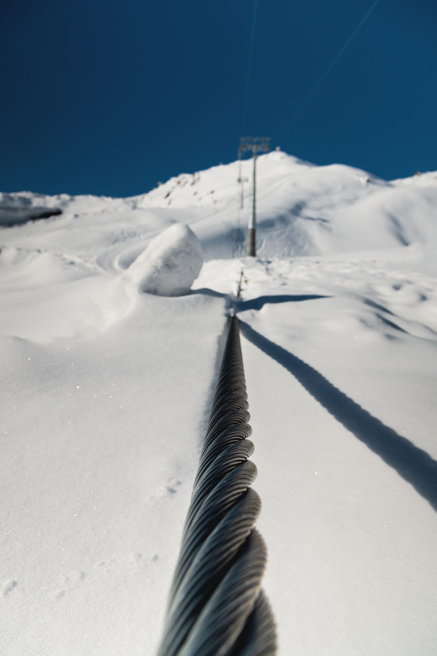 winter, snow, cold temperature, nature, environment, scenics - nature, beauty in nature, landscape, sky, mountain, day, no people, sunlight, land, cable, tranquility, mountain range, tranquil scene, blue, outdoors, travel, non-urban scene, ski equipment, ski, transportation, rope, frozen, piste, clear sky, white, snowcapped mountain, winter sports, sports, sunny, travel destinations, shadow