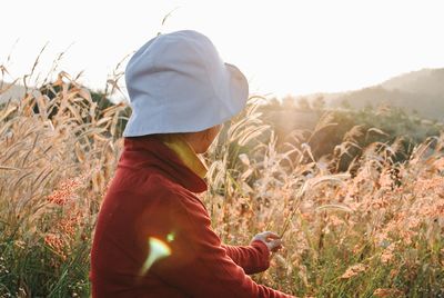 Side view of woman wearing hat while holding plants during sunset