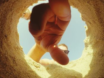 Close-up of hands on sand at beach against sky