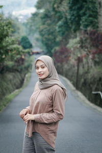 Portrait of woman standing on road against trees