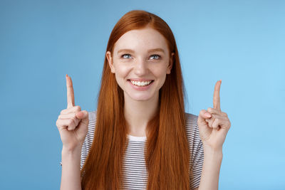 Portrait of smiling woman showing index finger against blue background