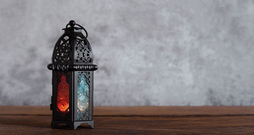 Illuminated lantern on table against wall