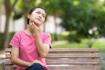 Young woman scratching neck while sitting on bench at park