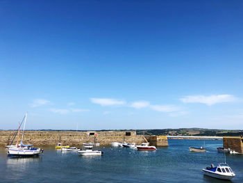 Sailboats moored on sea against blue sky