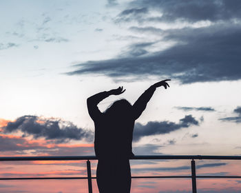 Silhouette woman with arms raised standing against sky during sunset