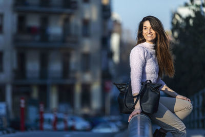 Smiling woman sitting on railing in city