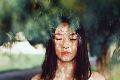 Close-up of young woman with eyes closed standing by tree at park