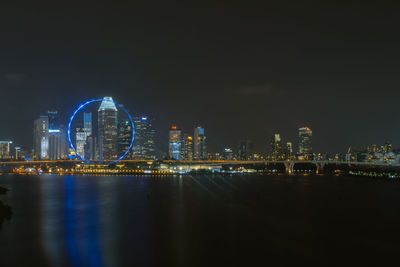 Illuminated city by river against sky at night