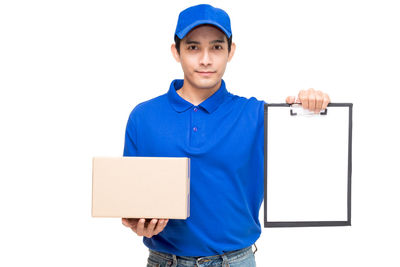 Portrait of salesman holding cardboard box and clipboard while standing against white background