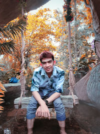 Portrait of young man sitting by tree against plants