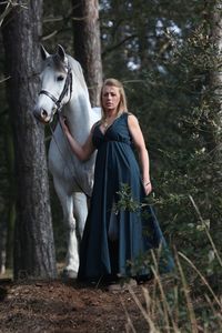 Full length of woman standing by horse in forest