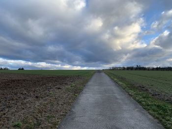 Empty road amidst field against sky