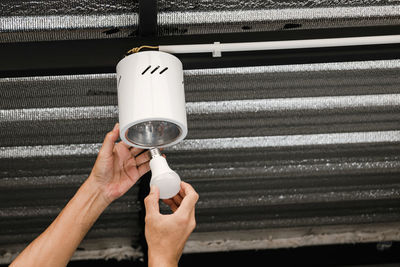 Close up human hand is installing an led light bulb in a circular ceiling lamp.