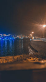 Illuminated city by sea against sky at night