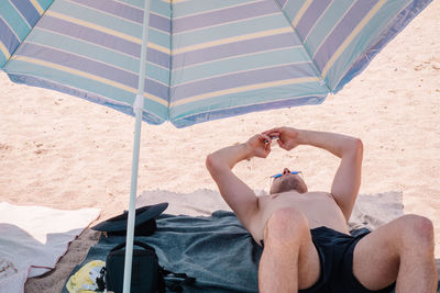 Shirtless man using mobile phone while relaxing at beach