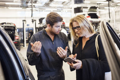Mechanic assisting customer in using mobile app at auto repair shop