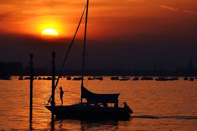 Silhouette woman standing on sailboats moored in lake against orange sky