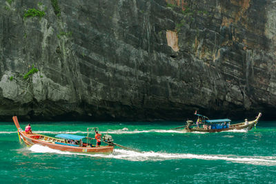 People on motorboats in sea against mountain