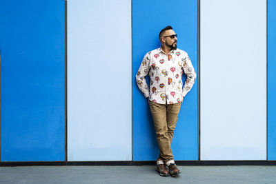 Bearded male leaning on colored wall with sunglasses, looking away