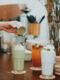 Cropped hand of person holding bottle over drink on table