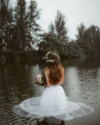 Rear view of woman sitting by lake against sky