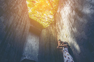 Low angle view of woman photographing with digital camera against wall