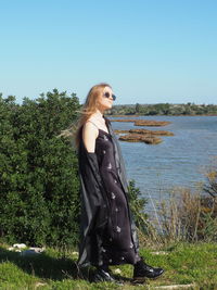 Side view of young woman standing by tree against clear sky