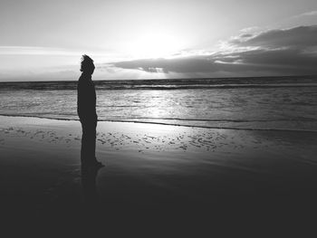Silhouette person standing on shore at beach against sky