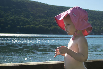 Topless girl in pink sun hat standing at lakeshore