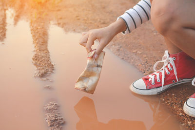 Low section of woman holding garbage over puddle on field