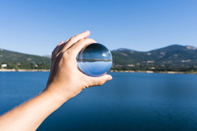 Midsection of person holding sunglasses against lake