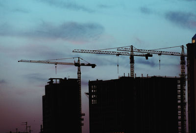 Silhouette crane by building against sky