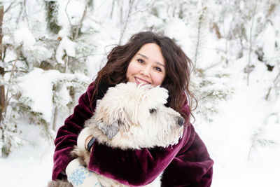 Portrait of smiling woman embracing dog in snow covered forest