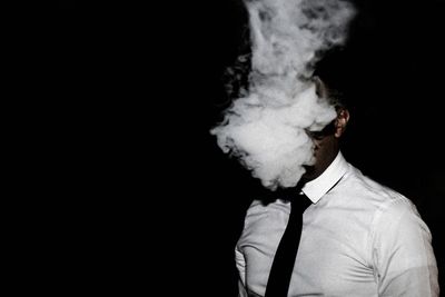 Close-up of man smoking against black background