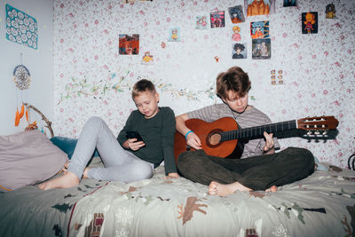 Children spend time, the girl plays the guitar, the boy uses a mobile phone.