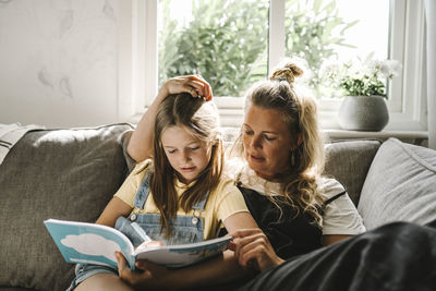 Daughter writing in book while sitting by mother on sofa at home