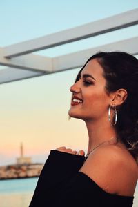 Portrait of smiling young woman looking away against sky