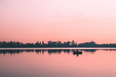 Person in boat on lake against clear sky during sunset