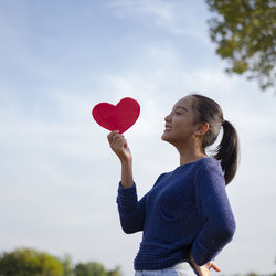 Rear view of woman holding heart shaped balloons against sky