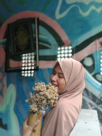 Smiling woman in hijab holding flower at home