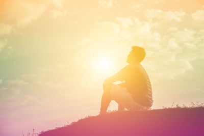 Rear view of man sitting against sky during sunset