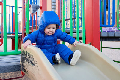 Cute toddler in a winter suit playing at the playground on the beach