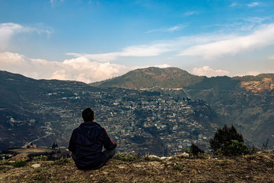 Rear view of woman sitting on mountain against sky