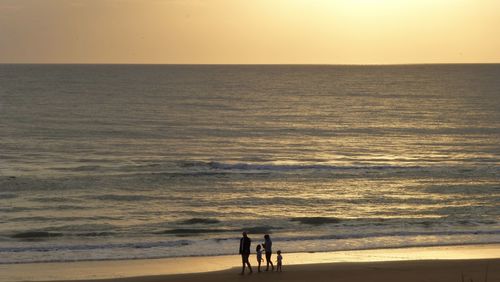 Silhouette people on beach against sky during sunset