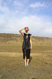 Full length of woman holding fruit while standing on field against sky