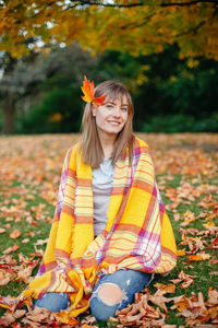 Portrait of smiling woman kneeling at park during autumn