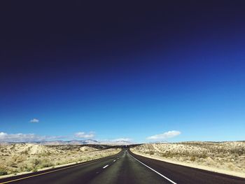 Empty road on field against clear blue sky